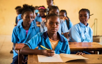Une fille lève les yeux de son bureau d'école alors qu'elle prend des notes en classe.