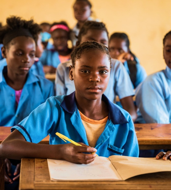 Une fille lève les yeux de son bureau d'école alors qu'elle prend des notes en classe.