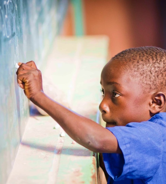 Un jeune garçon écrit sur un tableau noir dans une salle de classe.